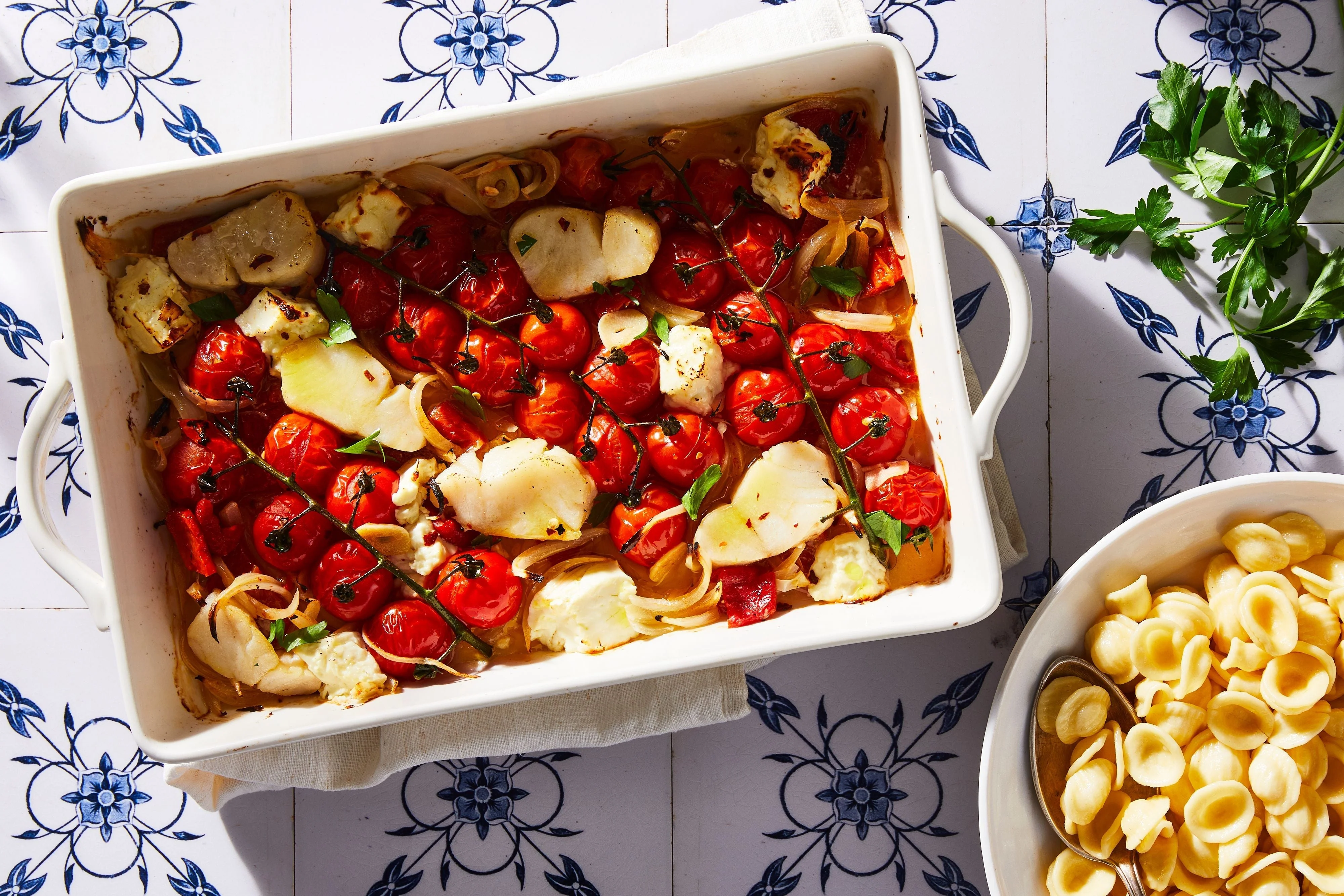 A 9x13-inch baking dish filled with roasted cherry tomatoes and a golden block of feta with bubbling olive oil and herbs on a bright kitchen counter
