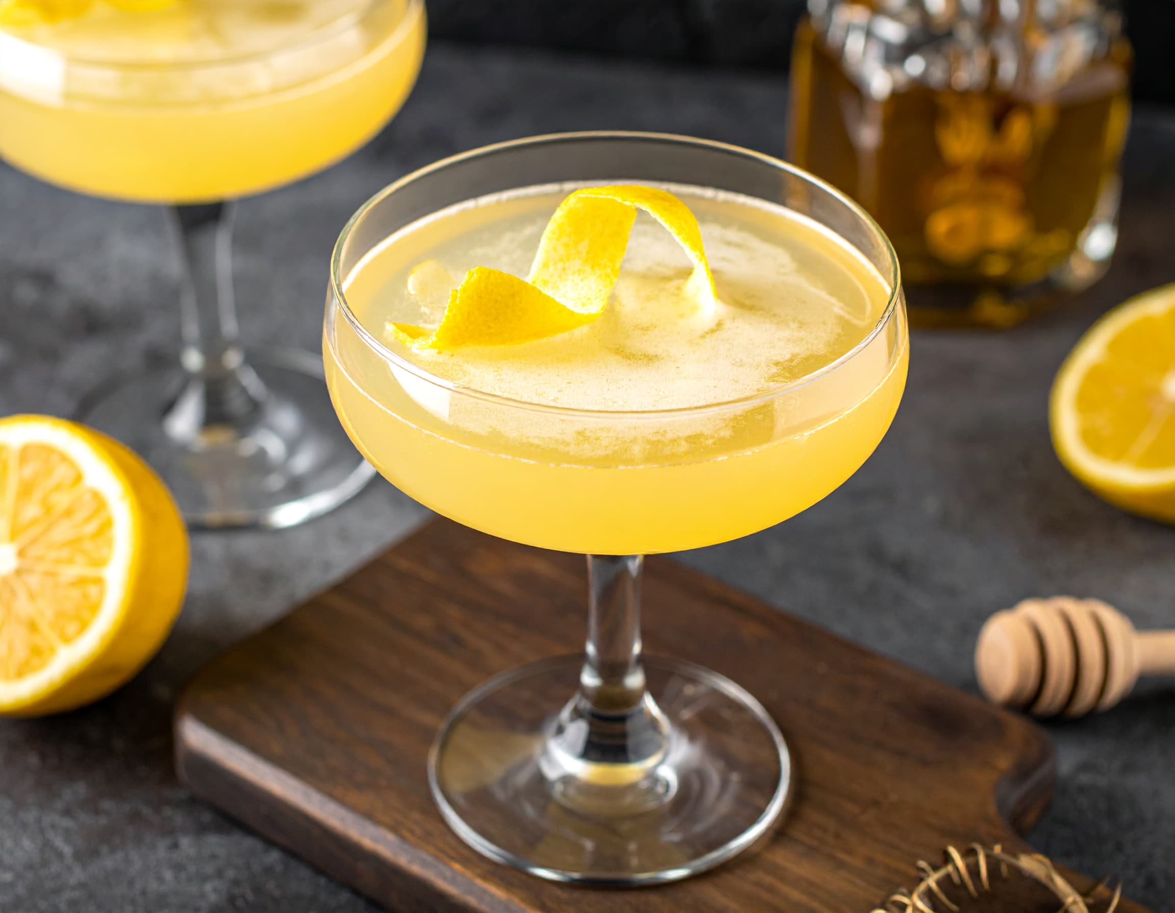 A Bee’s Knees cocktail in a chilled coupe glass with a lemon twist on the rim, set on a warm kitchen counter with soft natural light