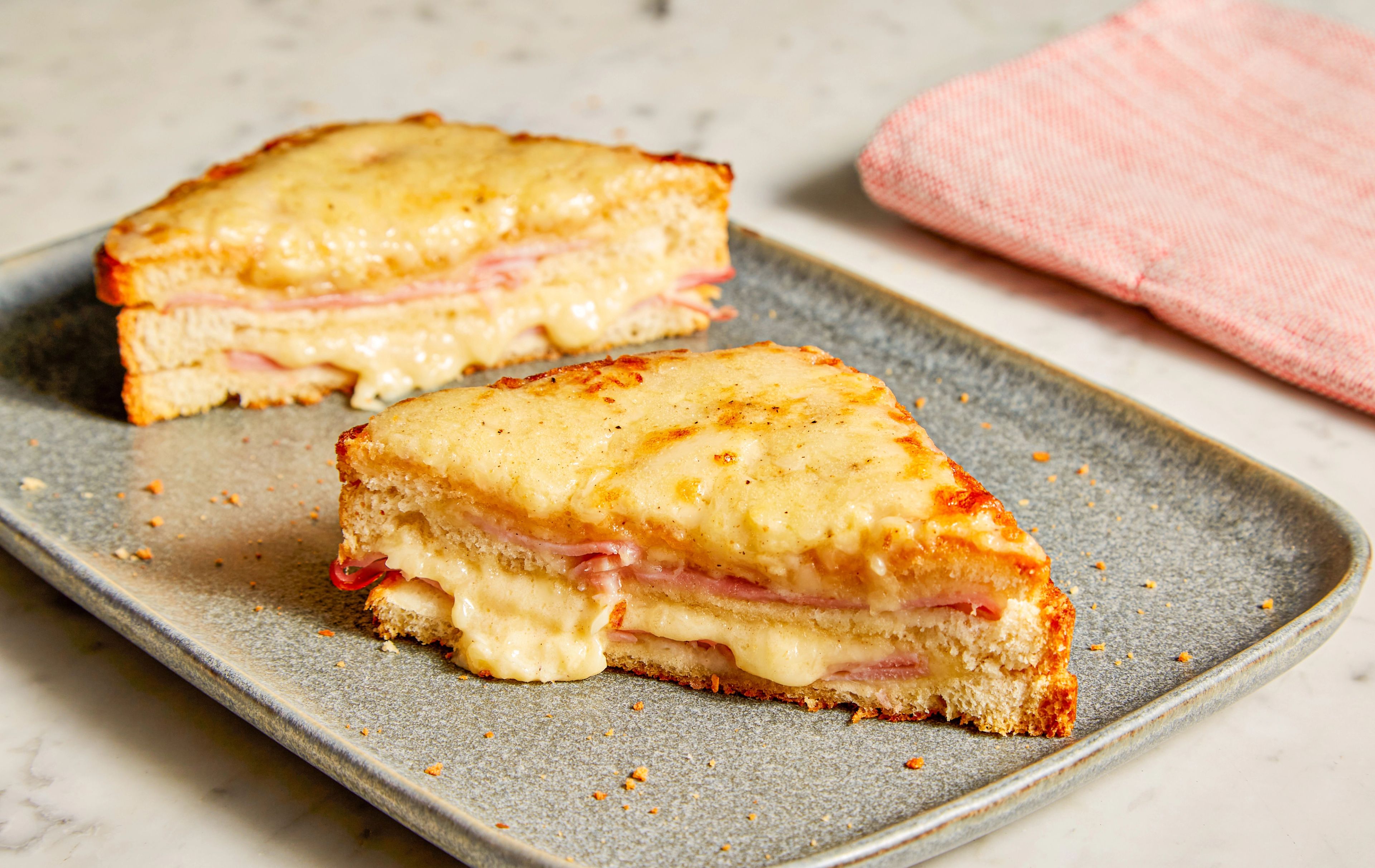 A Croque Monsieur on a baking sheet under an oven broiler, with melted cheese and béchamel bubbling and browning on top