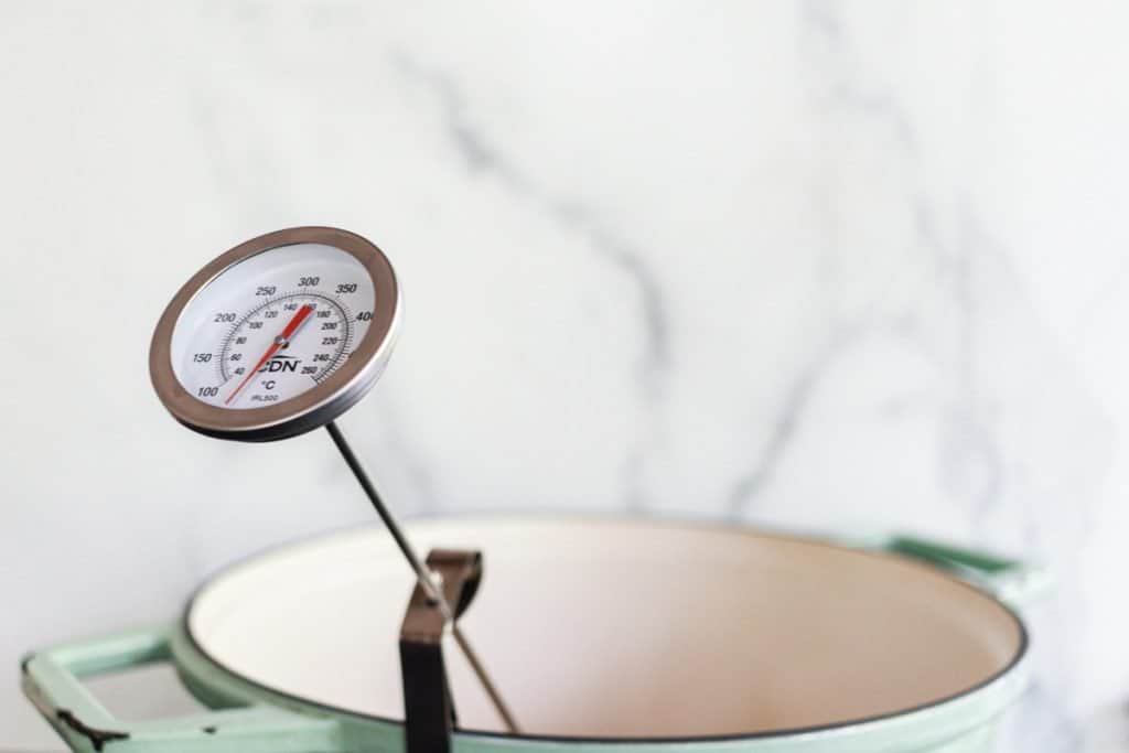 A Dutch oven filled with oil on a stovetop with a thermometer clipped to the side reading around 350°F
