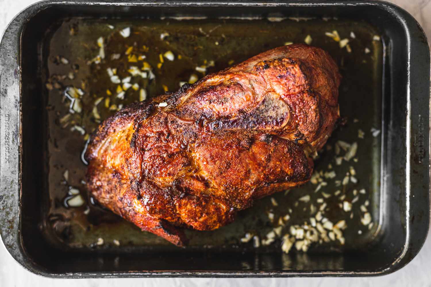 A Dutch oven filled with shredded pulled pork, glistening with juices, on a warm-toned kitchen counter with a wooden spoon nearby