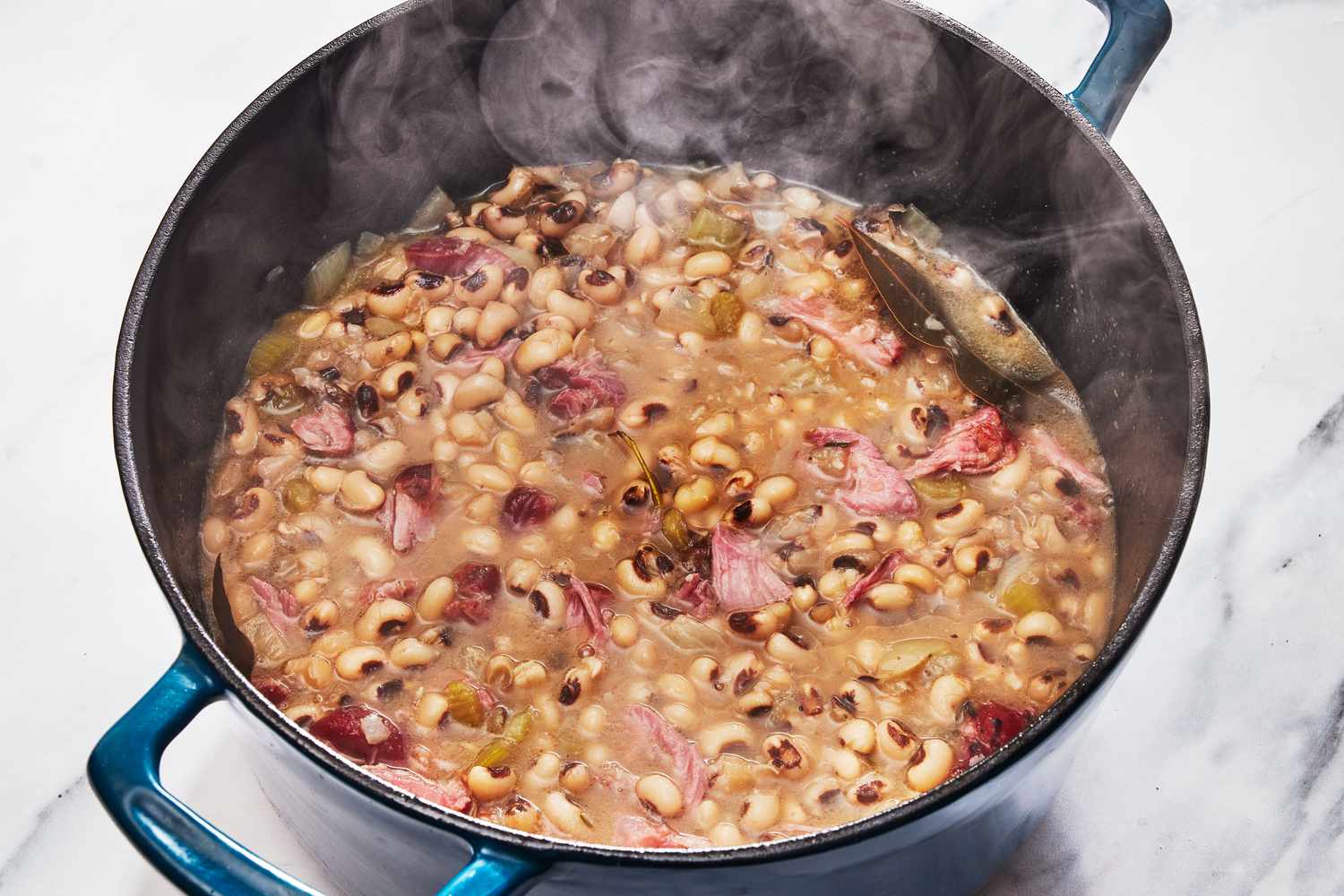 A Dutch oven filled with smoky black-eyed peas and bits of bacon, gently simmering on a stovetop with steam rising in a cozy home kitchen