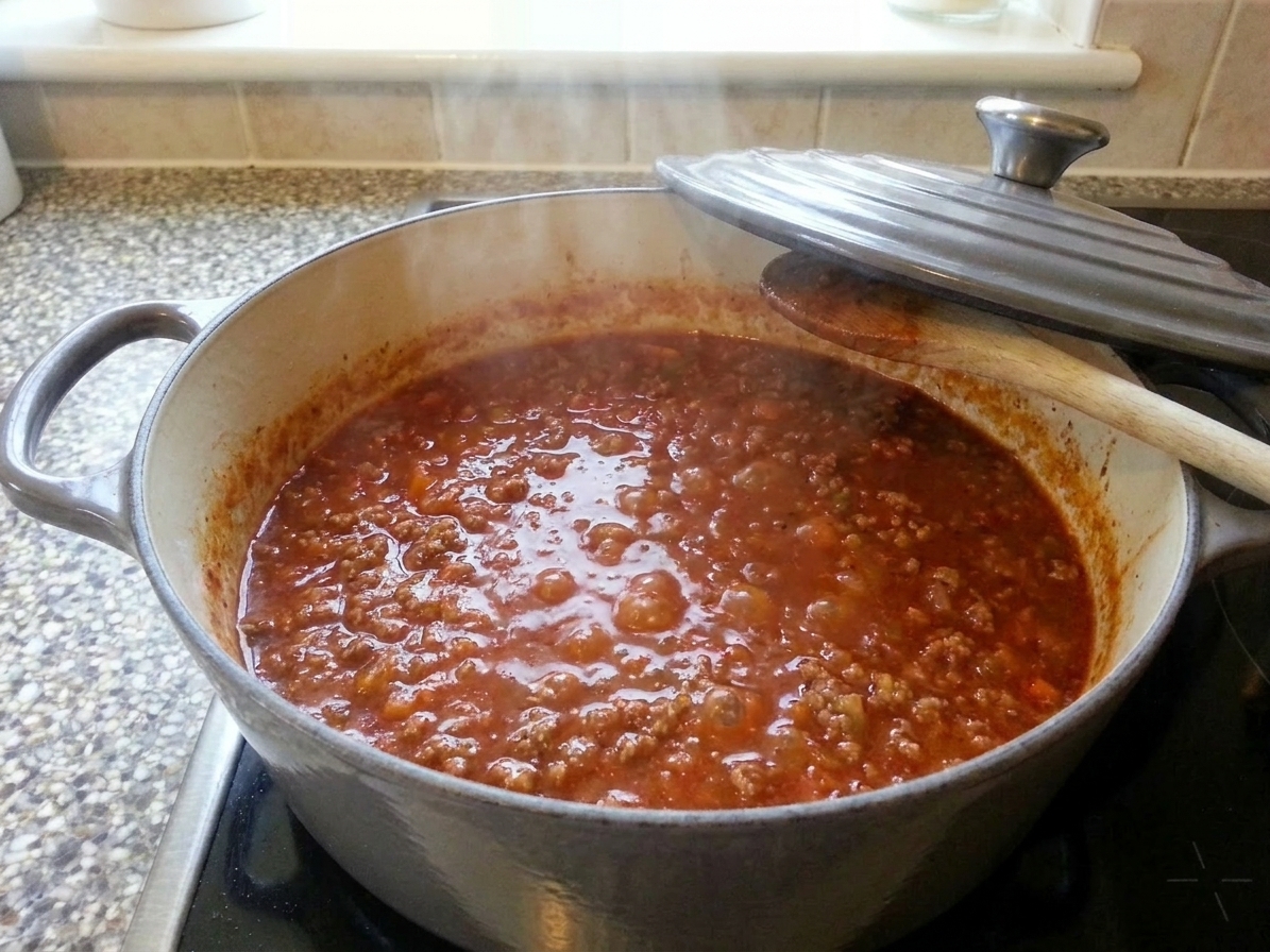 A Dutch oven of bolognese ragù gently simmering on a stovetop with the lid slightly ajar
