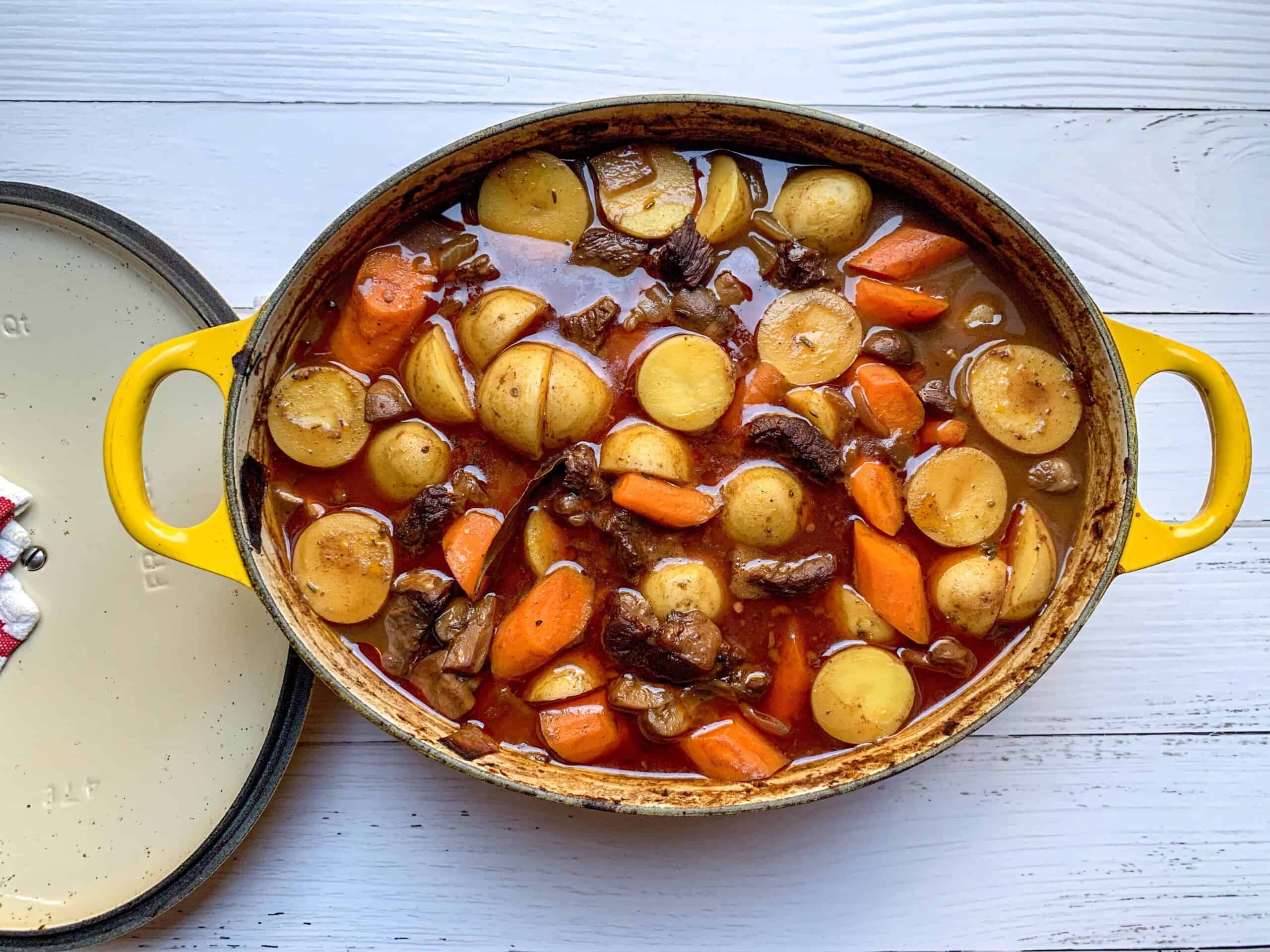 A Dutch oven on a stovetop filled with beef stew, showing tender beef chunks, carrots, and potatoes in a rich brown gravy with steam rising