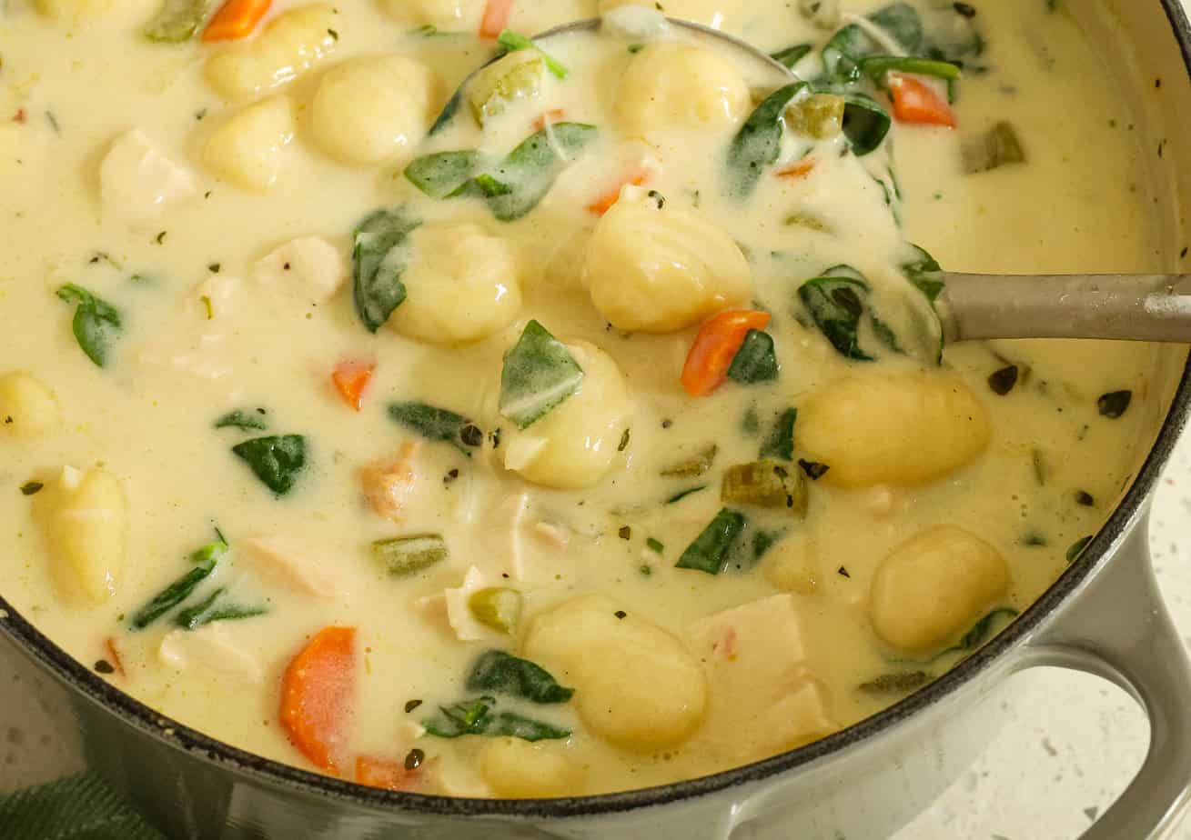 A Dutch oven on a stovetop with chicken gnocchi soup gently simmering, steam rising, and a wooden spoon resting on the rim