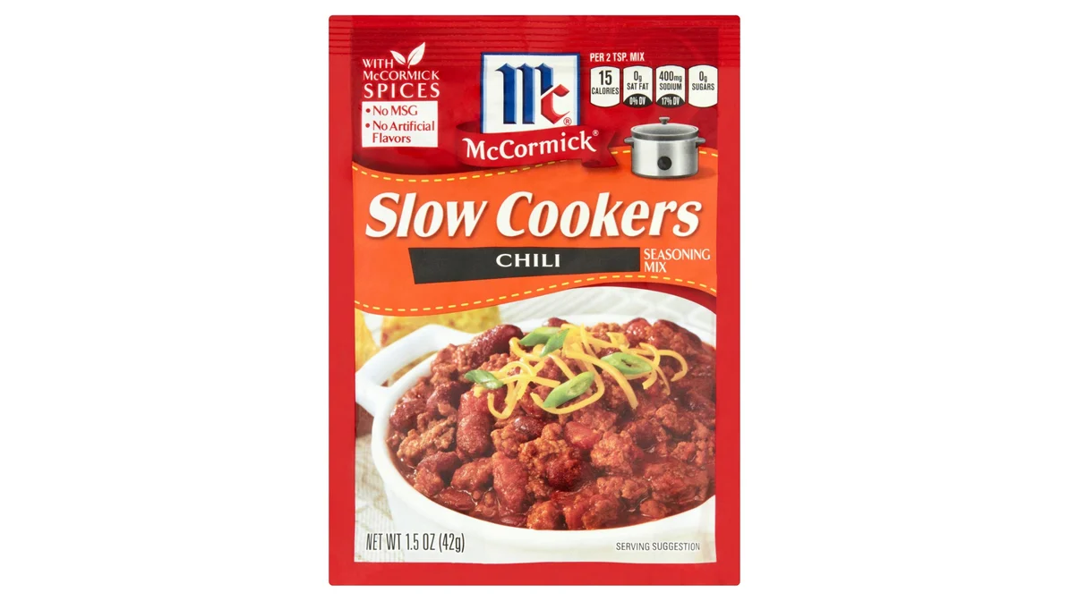 A McCormick chili seasoning mix packet on a kitchen counter next to small bowls of spices and canned tomatoes, ready for cooking