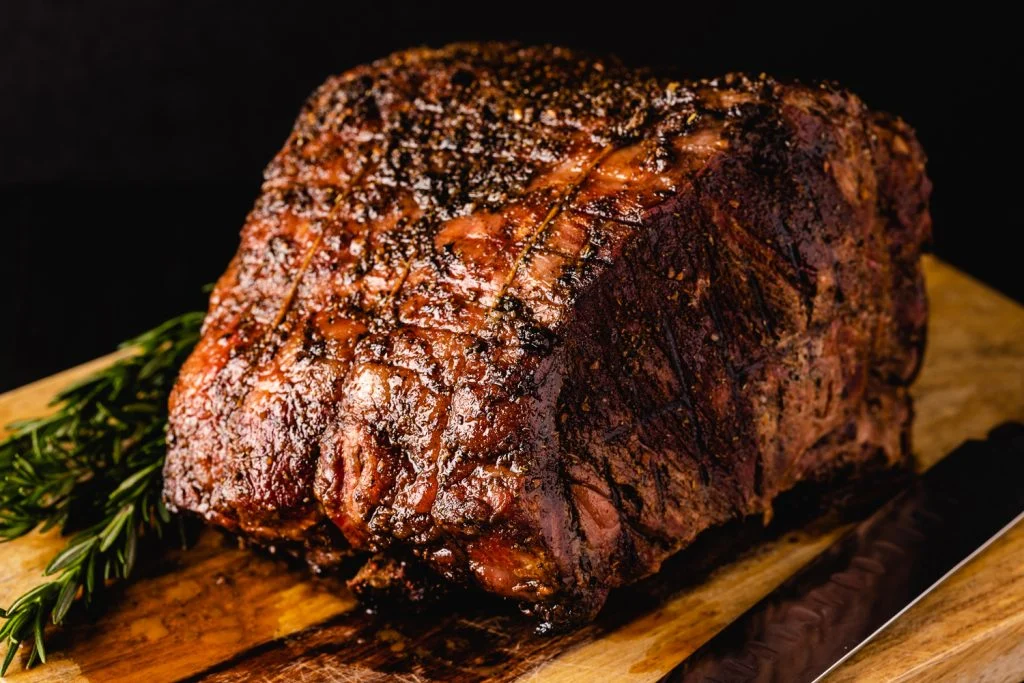 A New York strip loin roast evenly coated with salt and pepper on a sheet pan, resting on a kitchen counter in warm light