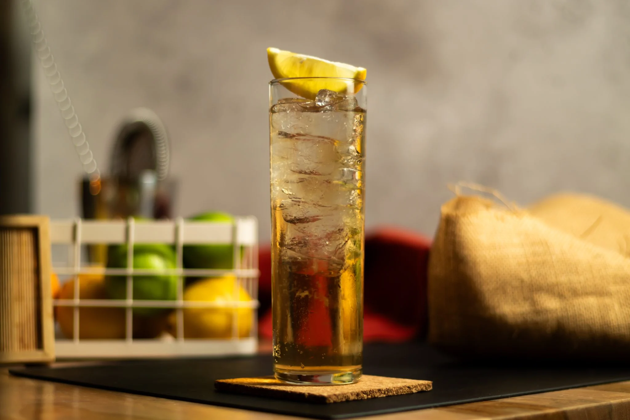 A Tripwire Hook cocktail in a rocks glass over a large clear ice cube, garnished with a lemon twist on a warm wood table with soft kitchen lighting