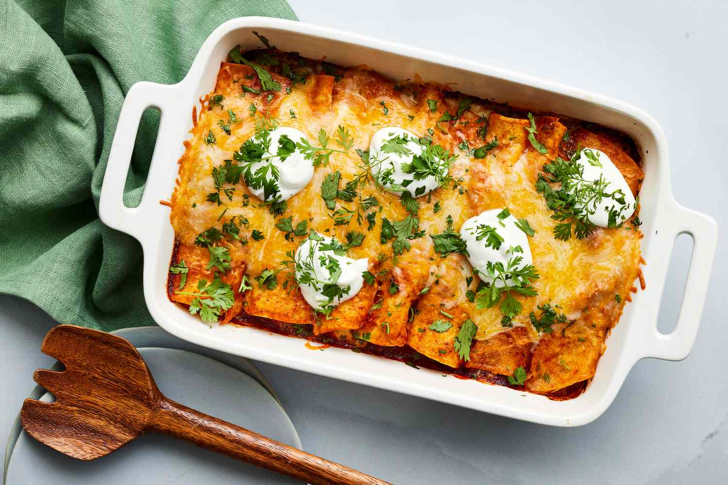 A baked chicken enchilada casserole in a glass baking dish with bubbling red enchilada sauce, melted cheese, and chopped cilantro on top, set on a warm kitchen counter with soft natural light