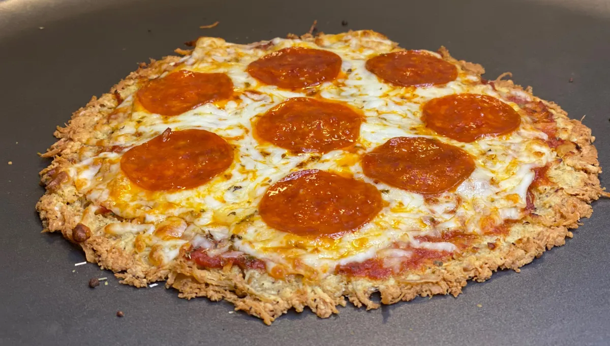 A baked chicken pizza crust topped with marinara, melted mozzarella, and basil on a parchment-lined baking sheet on a bright kitchen counter