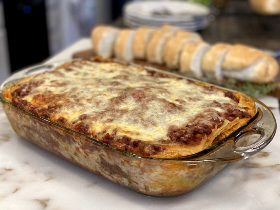 A baked ricotta lasagna in a glass baking dish with bubbling melted mozzarella and browned edges, resting on a wooden counter in a bright home kitchen