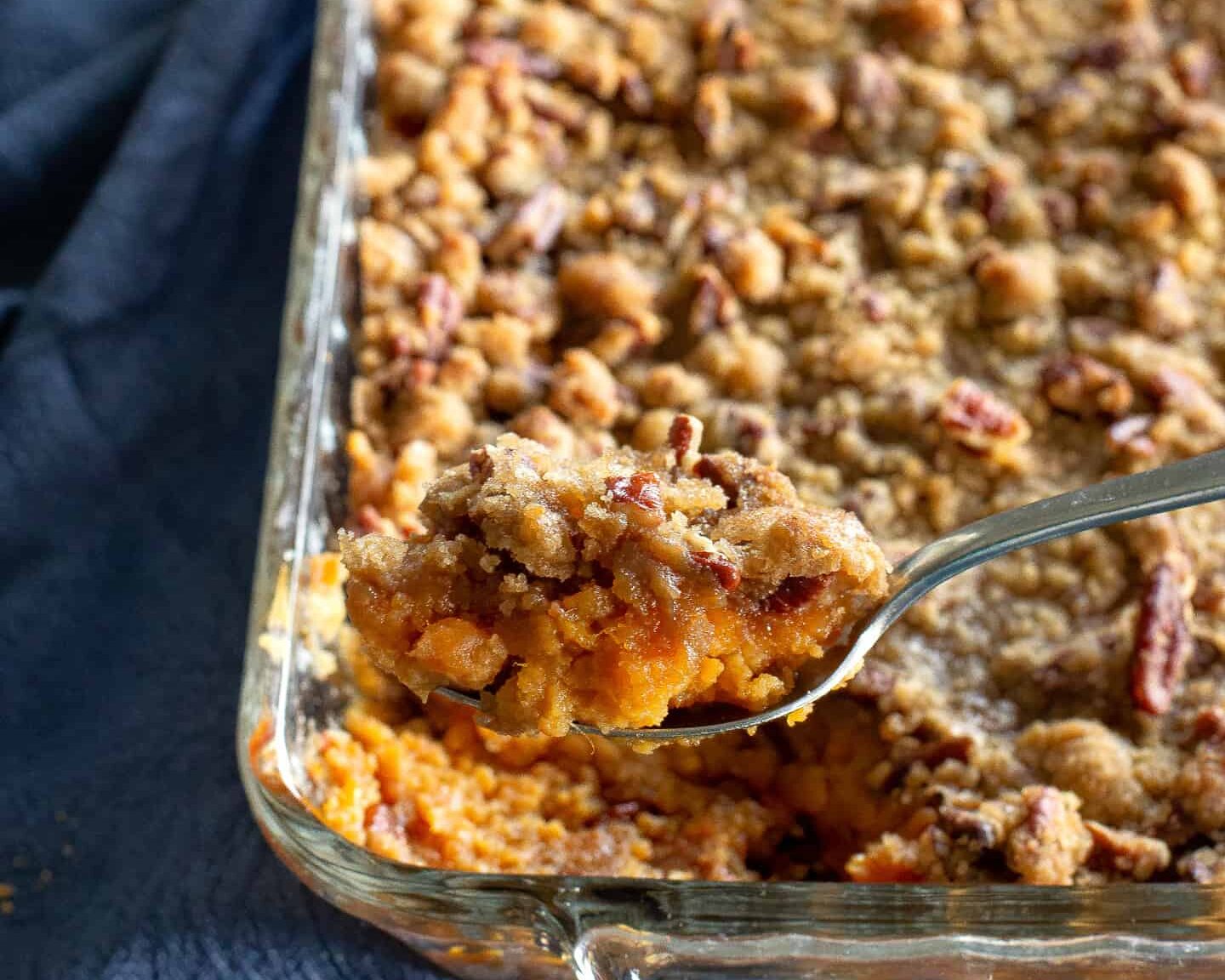 A baked sweet potato casserole in a white ceramic dish with a golden brown pecan streusel topping, set on a warm kitchen counter with soft natural light