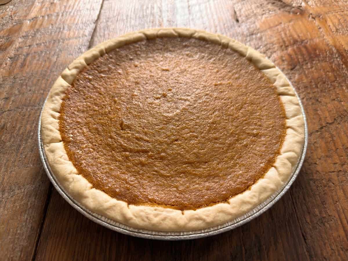 A baked sweet potato pie in a glass pie dish with a small crack across the center and browned edges under warm kitchen light