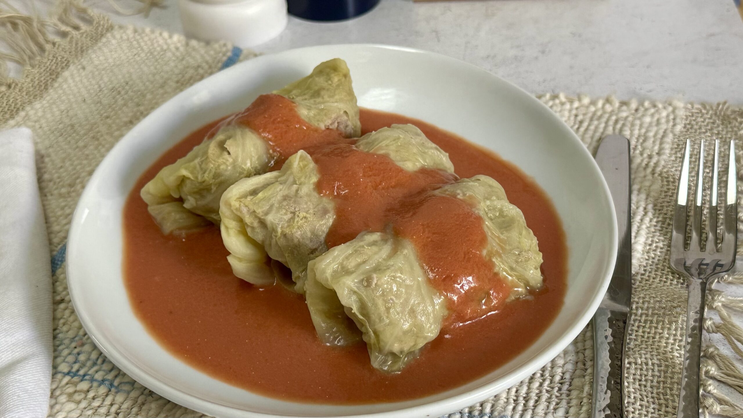 A baking dish filled with Polish golumpki cabbage rolls nestled in tangy tomato sauce, fresh parsley sprinkled on top, warm kitchen lighting