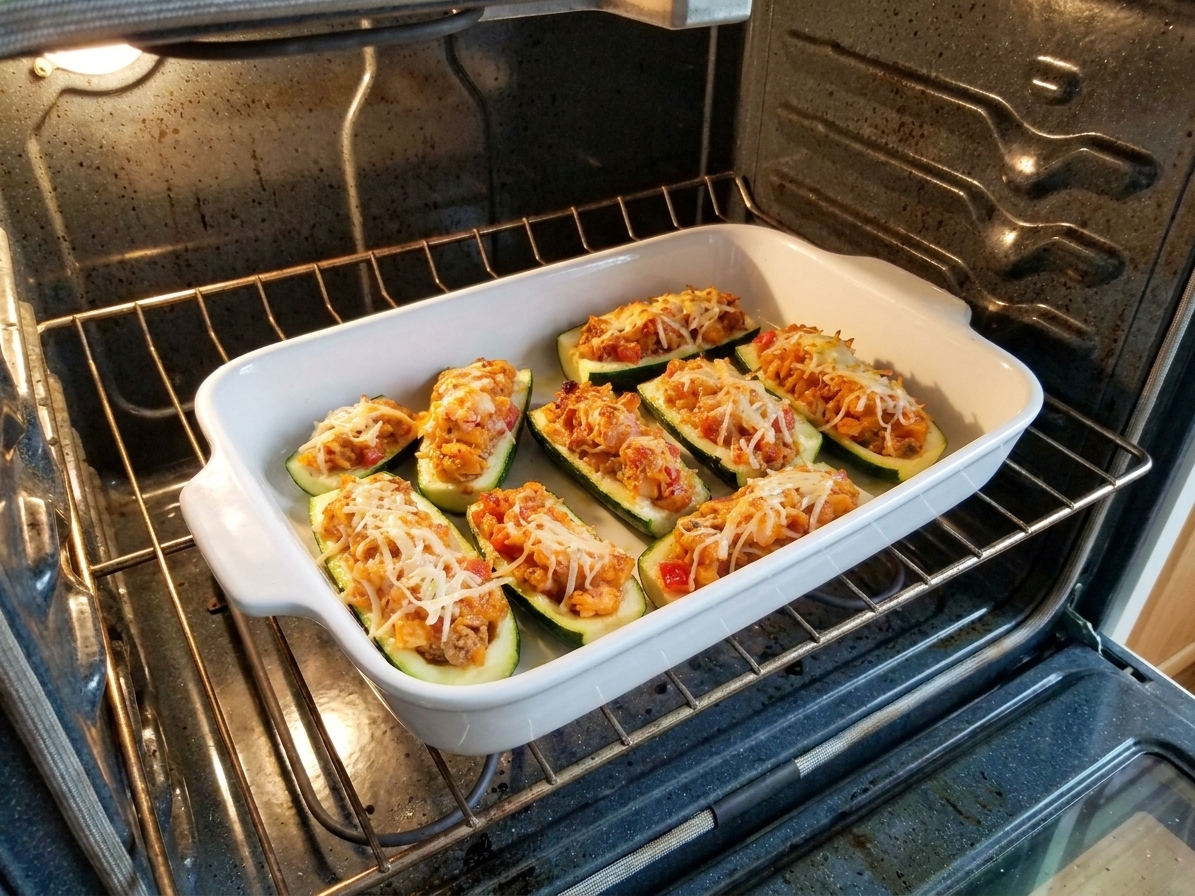 A baking dish of zucchini boats on the middle rack of an oven with cheese melting and lightly bubbling