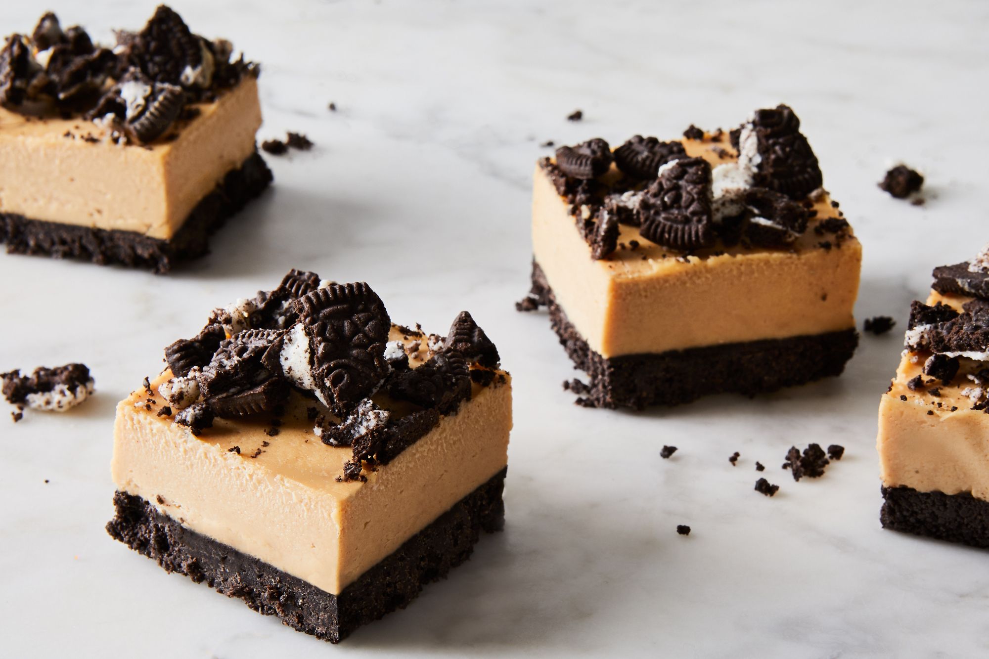 A baking dish on a kitchen counter with a dark Oreo cookie crumb crust being pressed in evenly with the back of a measuring cup