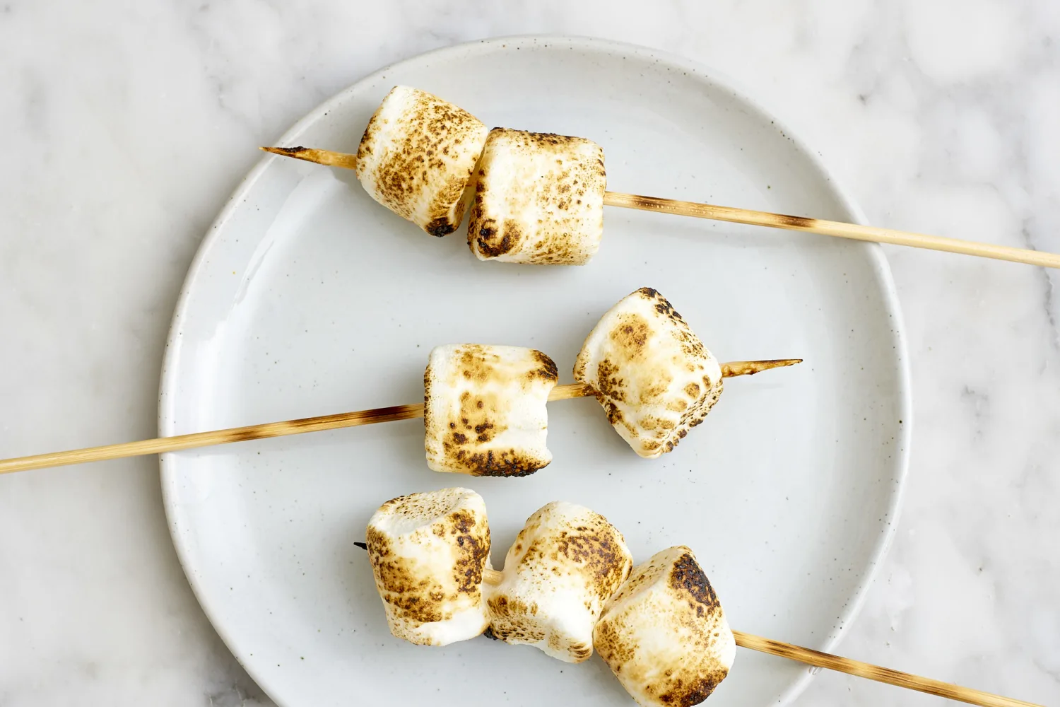 A baking pan under an oven broiler with marshmallows turning golden on top of s’mores bars, kitchen oven light on