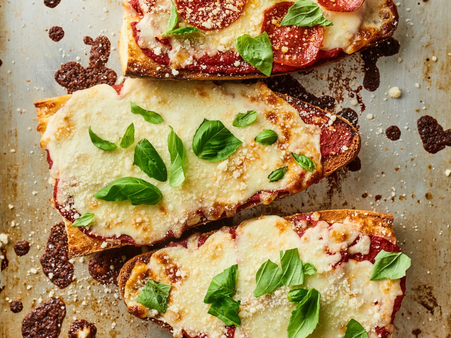 A baking sheet of French bread pizza halves topped with bubbling mozzarella, pepperoni, and browned edges, set on a warm-toned kitchen counter with soft natural light