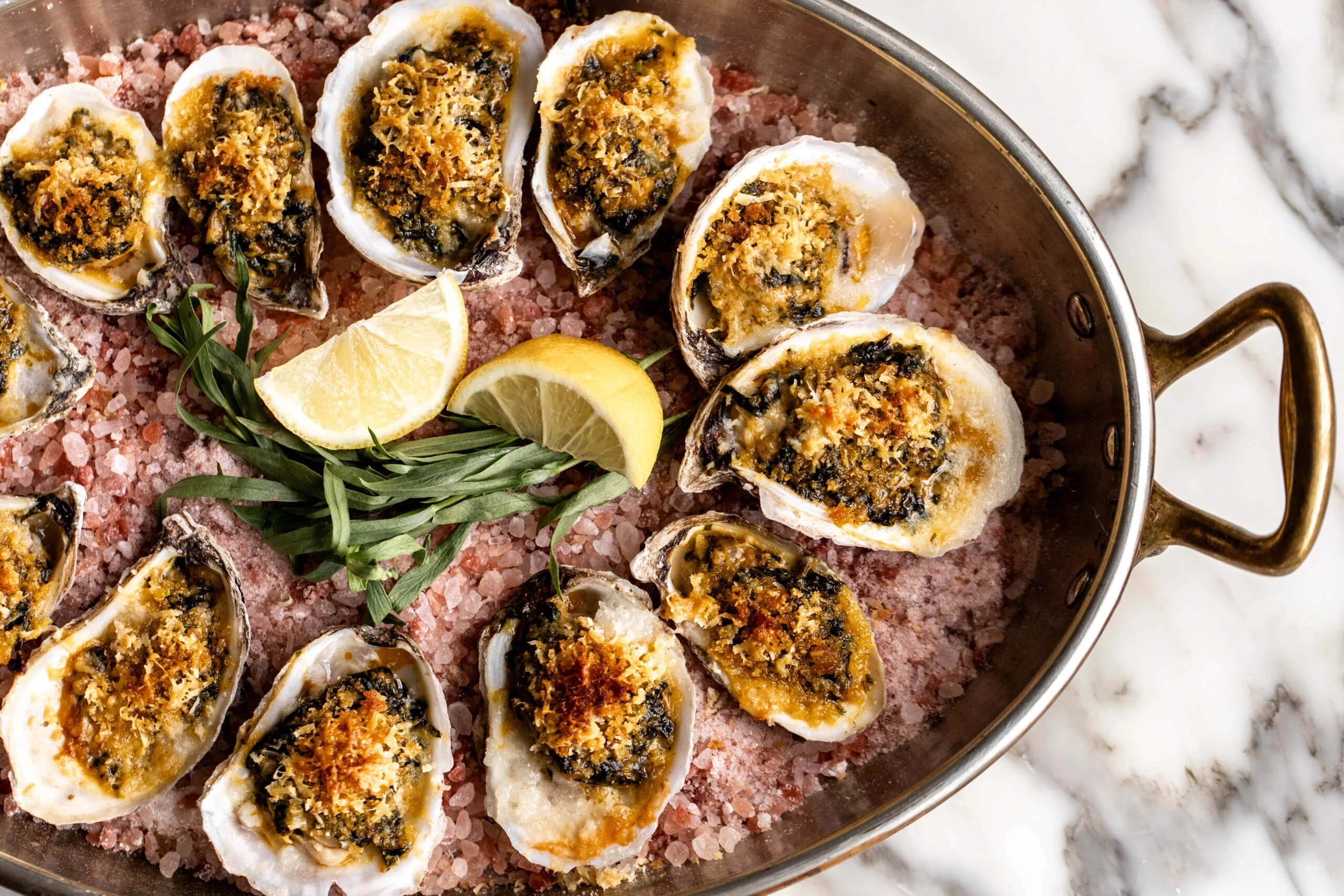 A baking tray of Oysters Rockefeller on a bed of rock salt, each oyster topped with a golden spinach herb crust