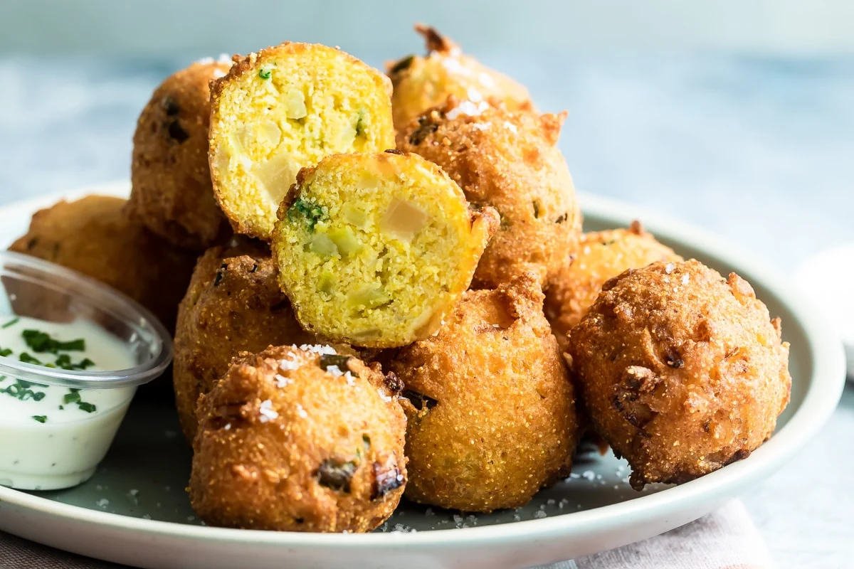 A basket lined with a cloth napkin holding golden-brown hush puppies with crisp, craggy edges on a wooden table