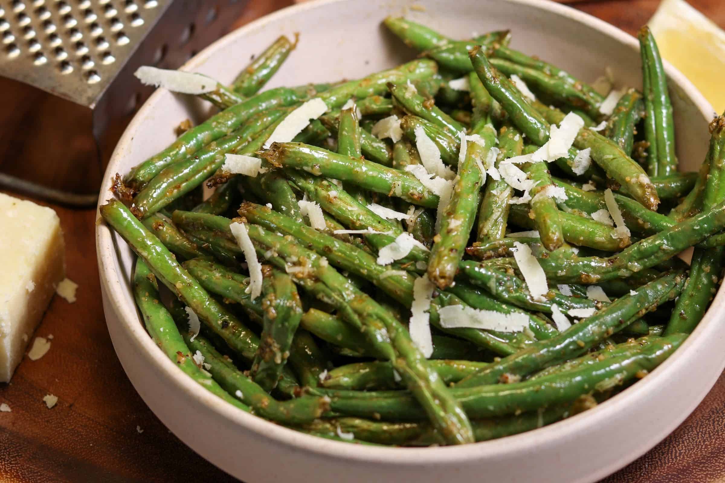 A basket of an air fryer pulled open on a bright kitchen counter, filled with crisp-tender garlic parmesan green beans with browned edges