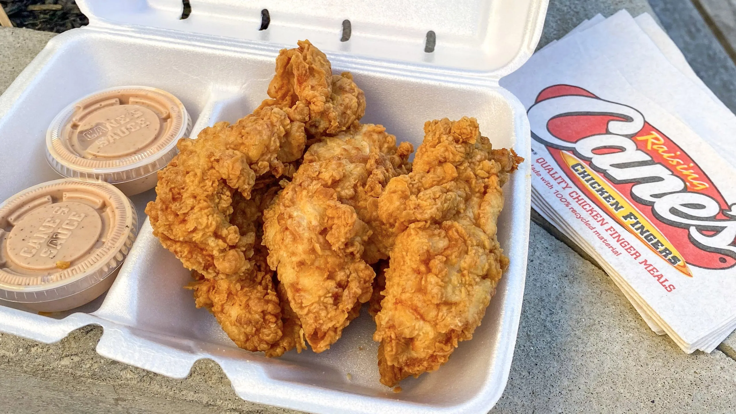 A basket of golden crispy chicken tenders with crinkle-cut fries, Texas toast, and a small cup of creamy dipping sauce on a casual table
