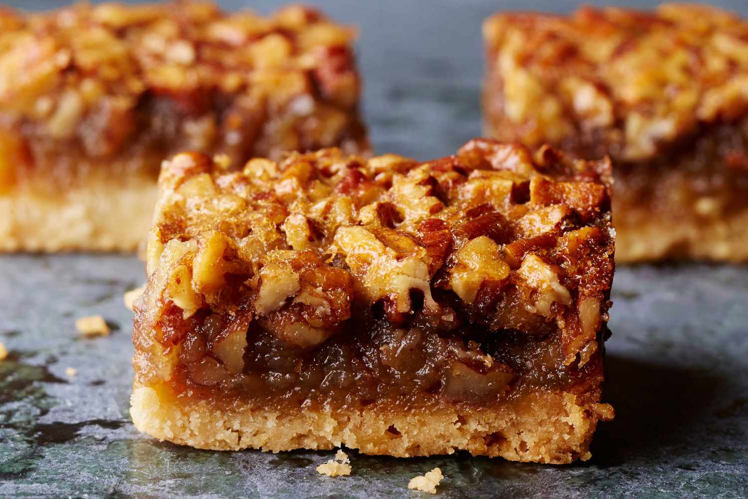 A batch of pecan pie bars in a metal baking pan with a glossy pecan topping and neatly cut squares.