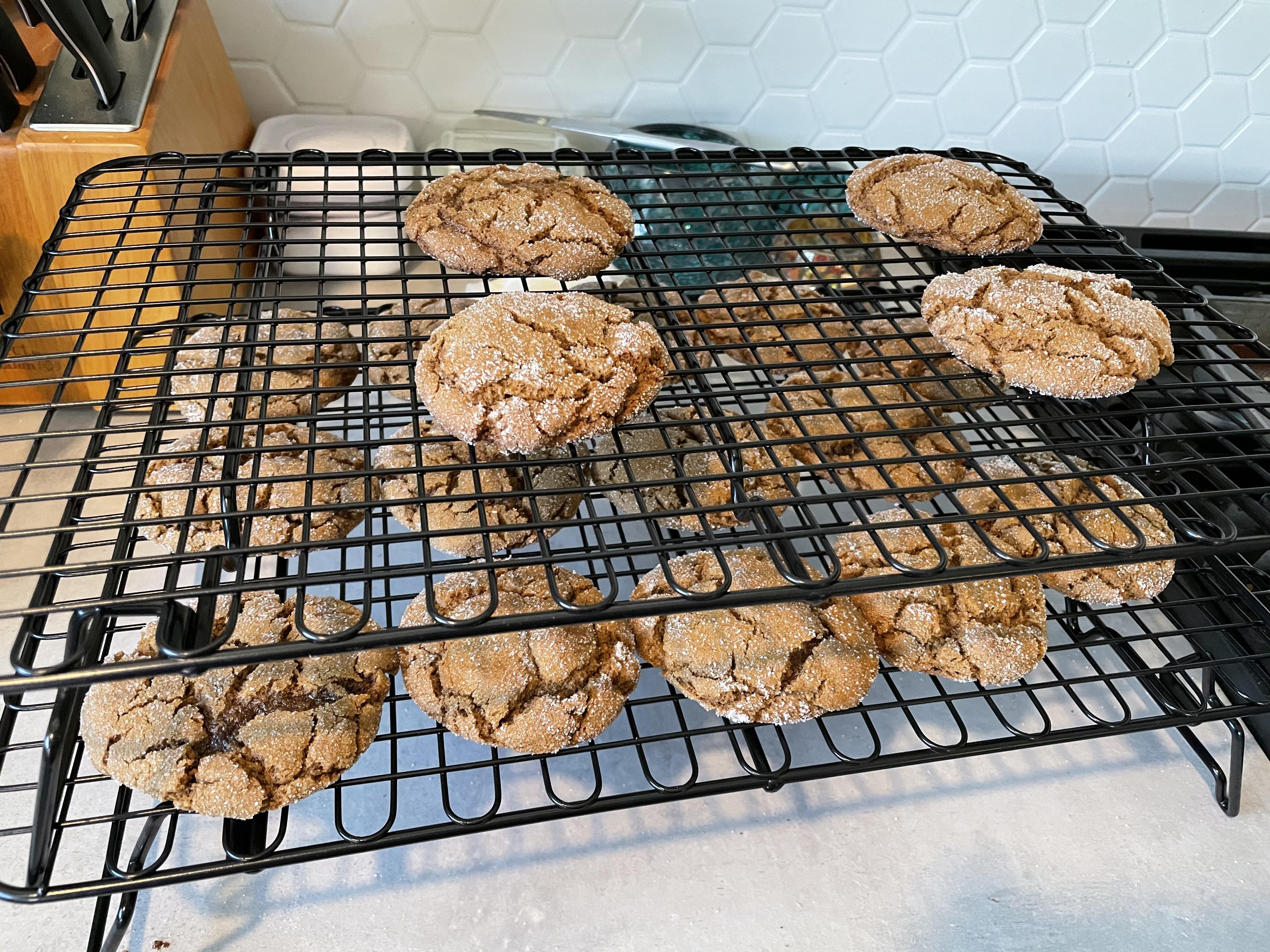 A batch of sugar-crackled molasses cookies cooling on a wire rack on a light stone kitchen counter with warm natural light