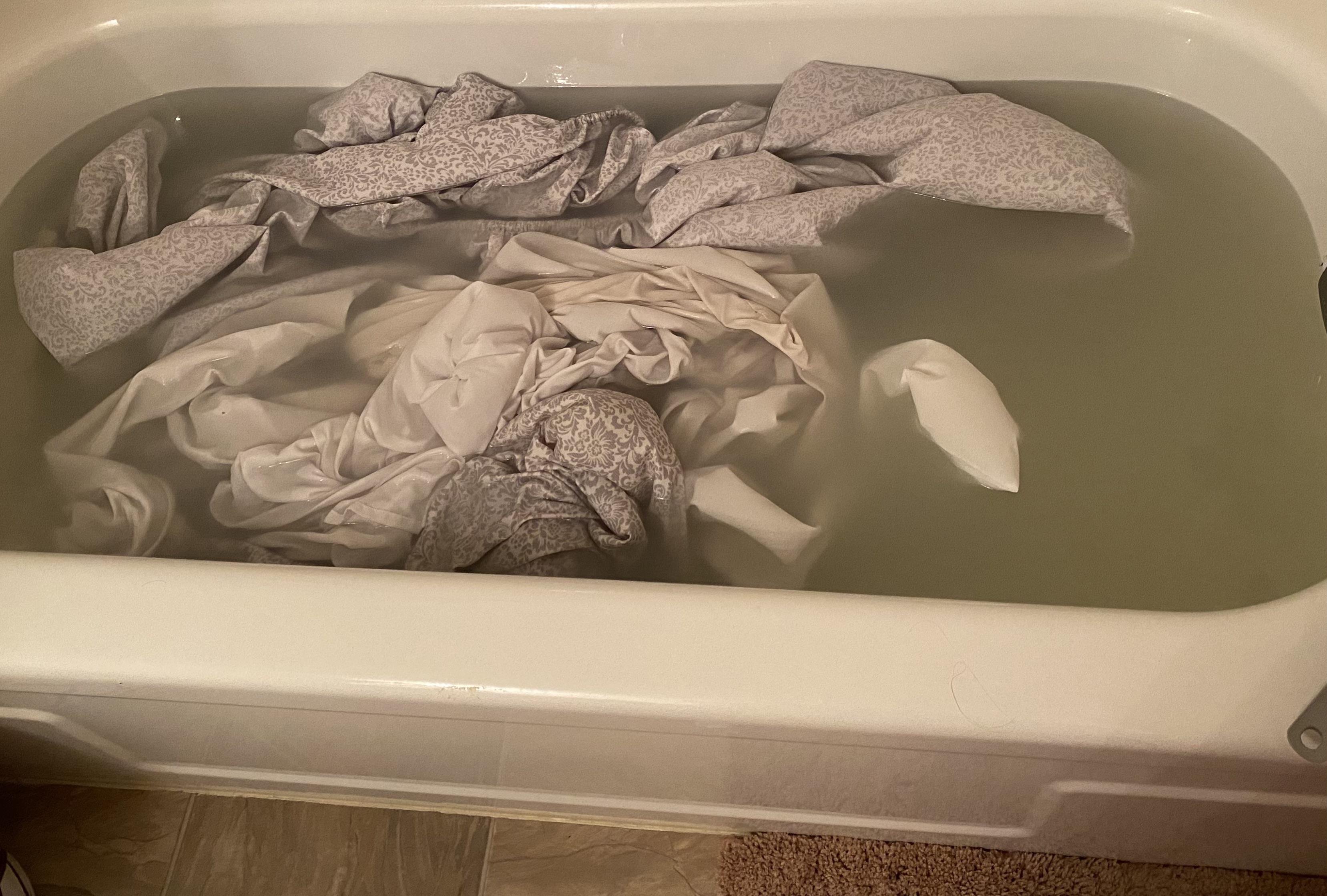A bathtub being filled with steaming hot water while folded towels sit ready to be submerged on the tub edge