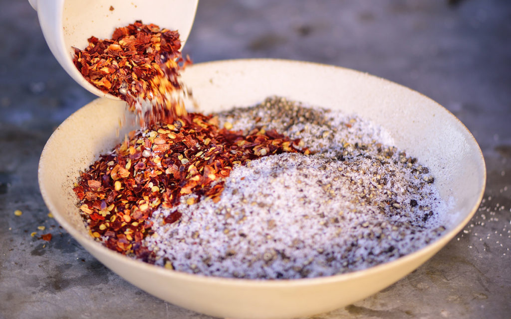 A beef brisket coated in a smoky spice rub on a wooden cutting board, with a small bowl of remaining rub nearby