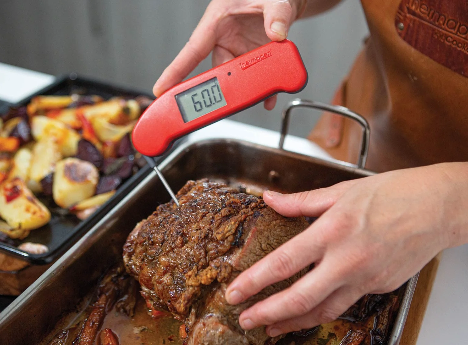 A beef roast in a roasting pan being quickly checked with a thermometer inserted into the thickest part
