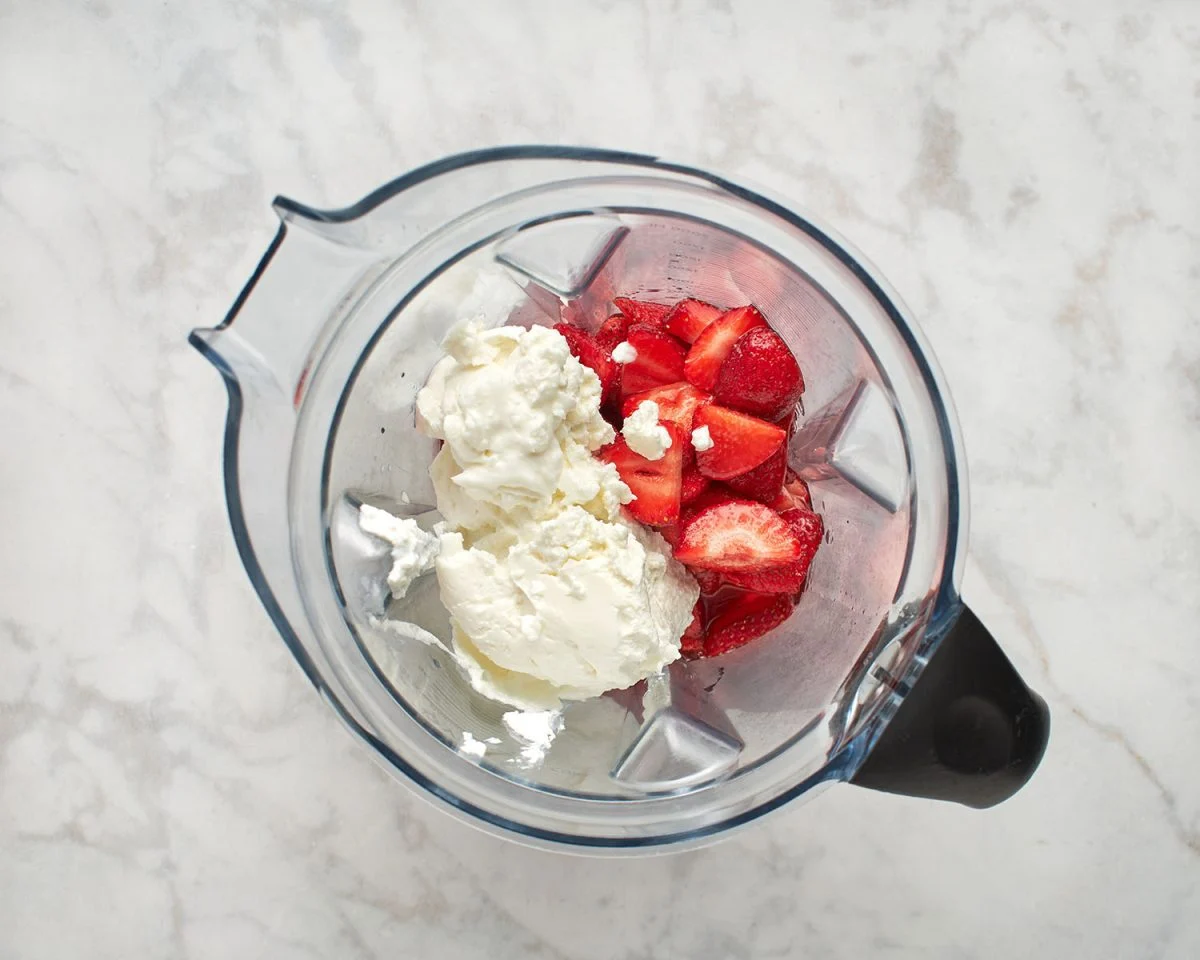A blender jar filled with a smooth pink strawberry yogurt mixture on a kitchen counter