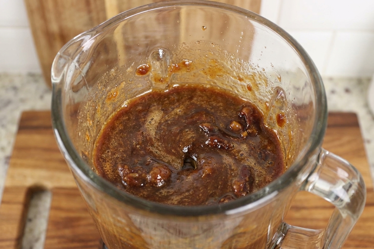 A blender jar filled with blended date caramel mid-puree on a bright kitchen counter