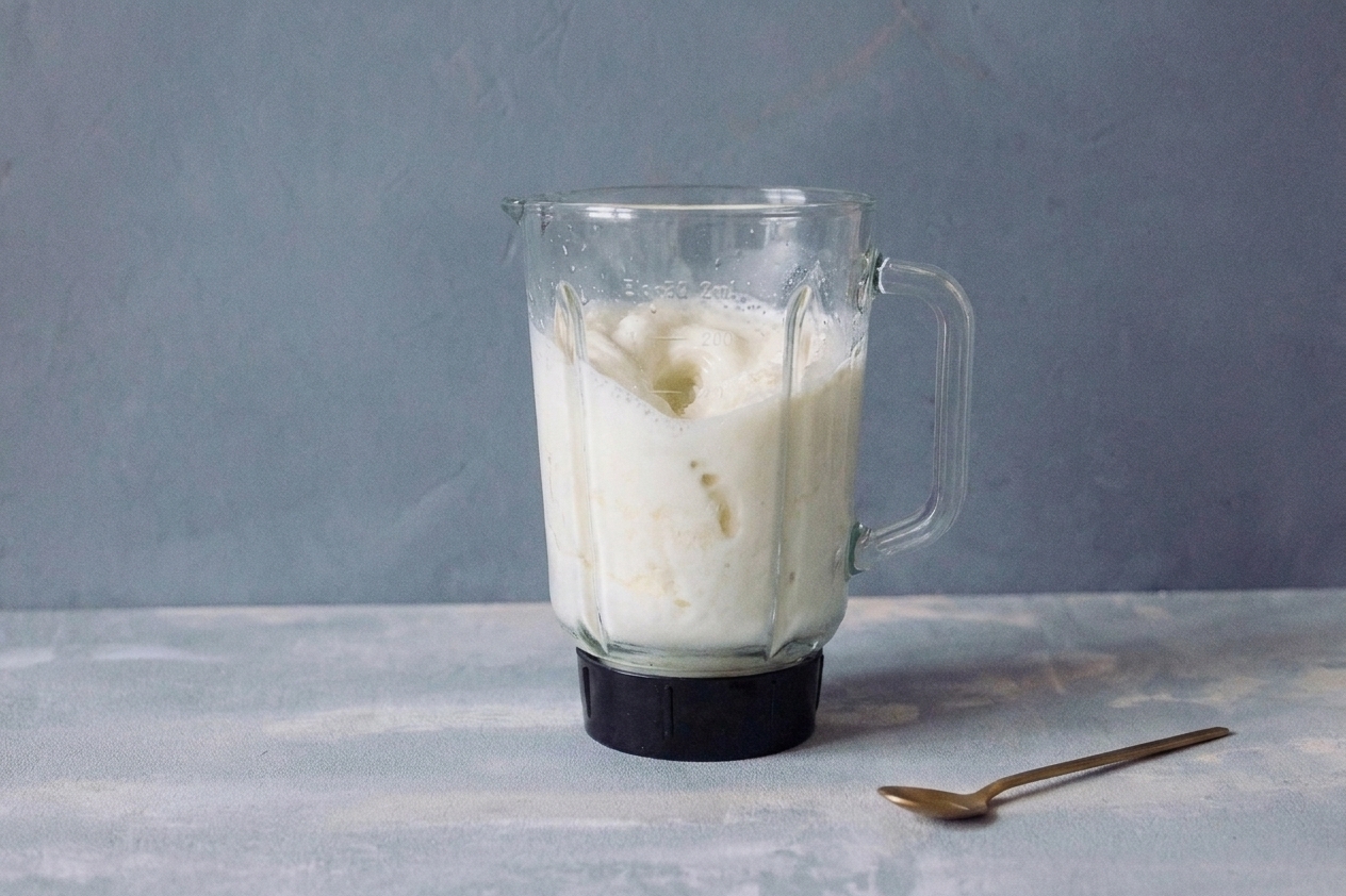A blender jar filled with vanilla ice cream and milk mid-blend on a bright kitchen counter