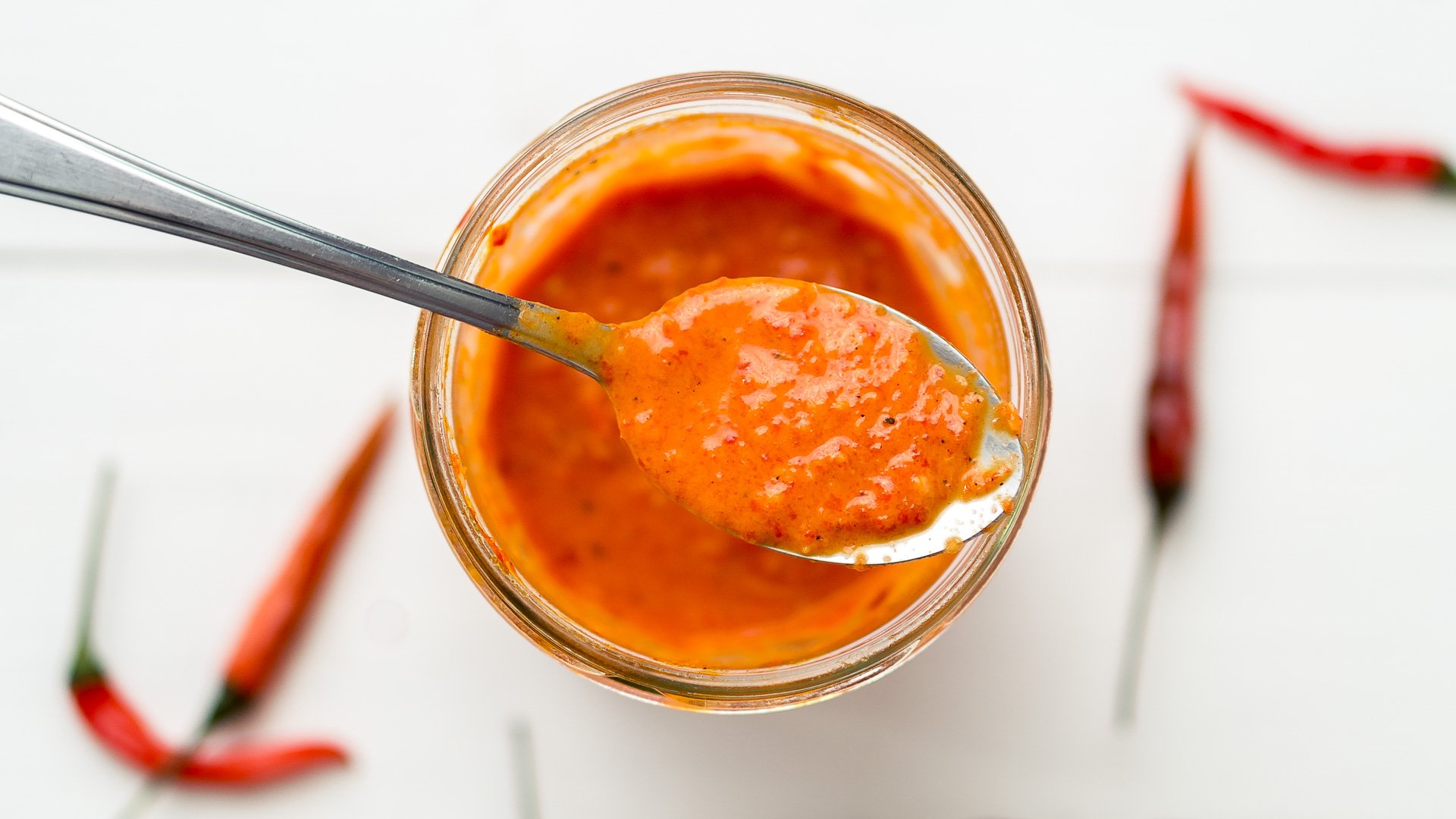 A blender jar filled with vivid red piri piri sauce on a bright kitchen counter, ready to be poured