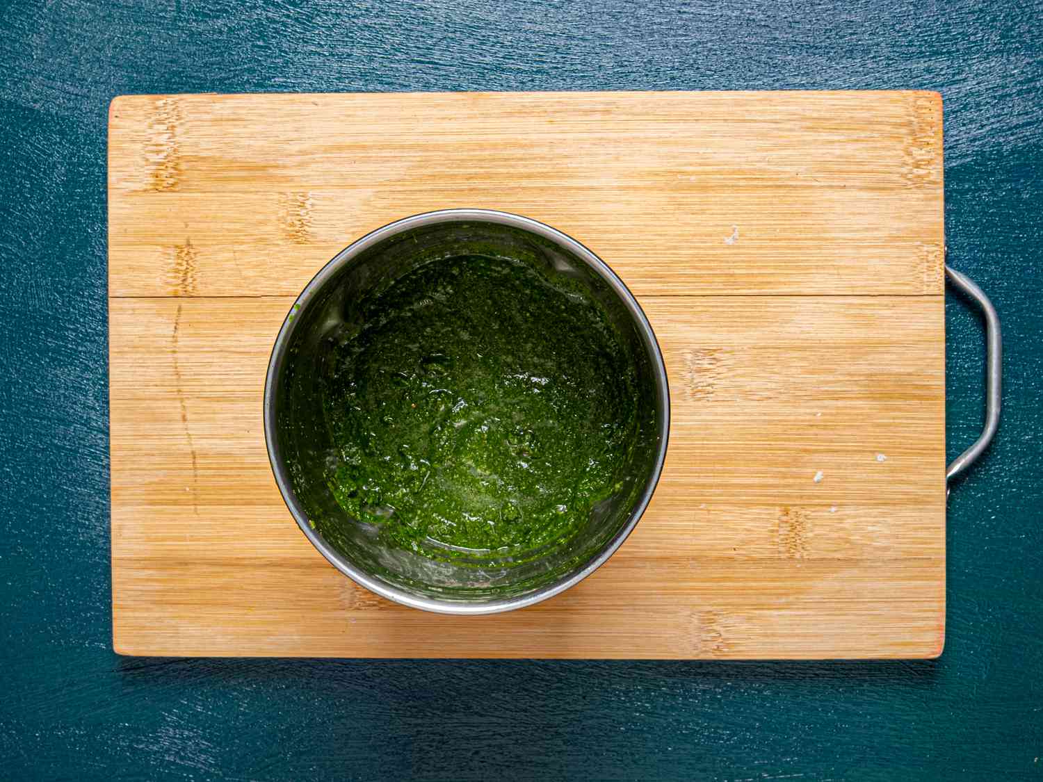 A blender jar with mint and cilantro being blended into a bright green pani mixture on a kitchen counter