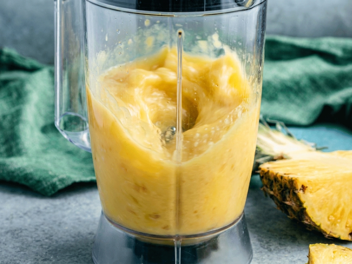 A blender running on a kitchen counter with pineapple smoothie swirling inside the jar