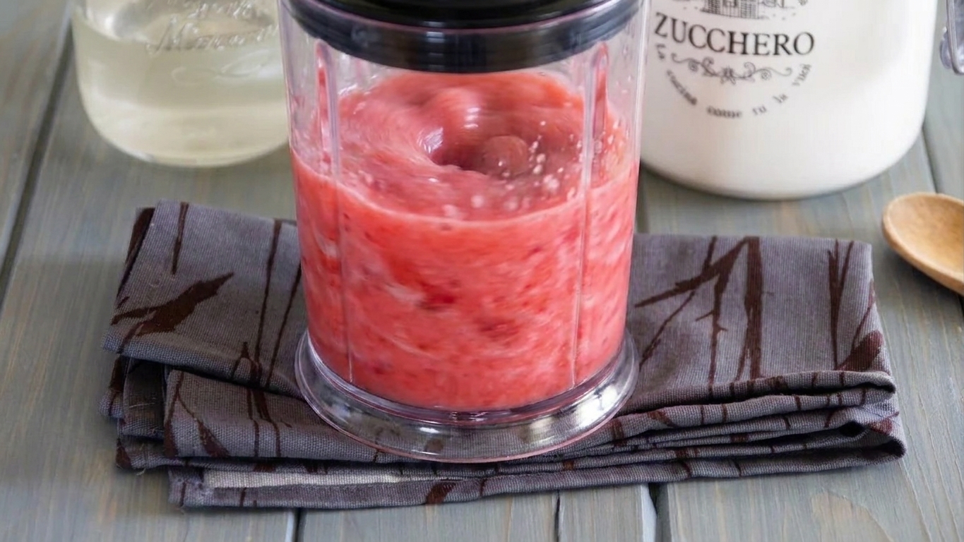 A blender running with a bright pink strawberry daiquiri mixture swirling into a smooth slush