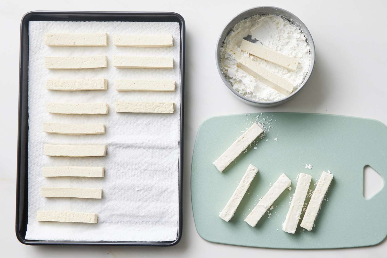 A block of tofu pressed between paper towels under a plate on a kitchen counter