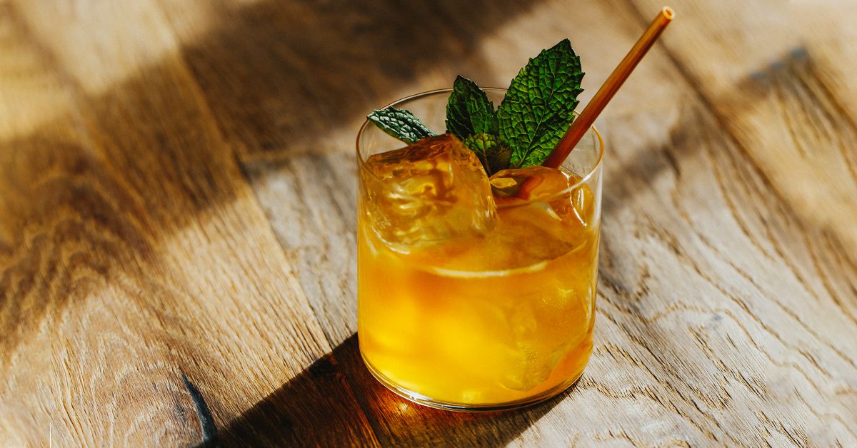 A bourbon smash cocktail in a short rocks glass with crushed ice, fresh mint sprig, and a lemon wedge on a wooden kitchen counter in warm natural light