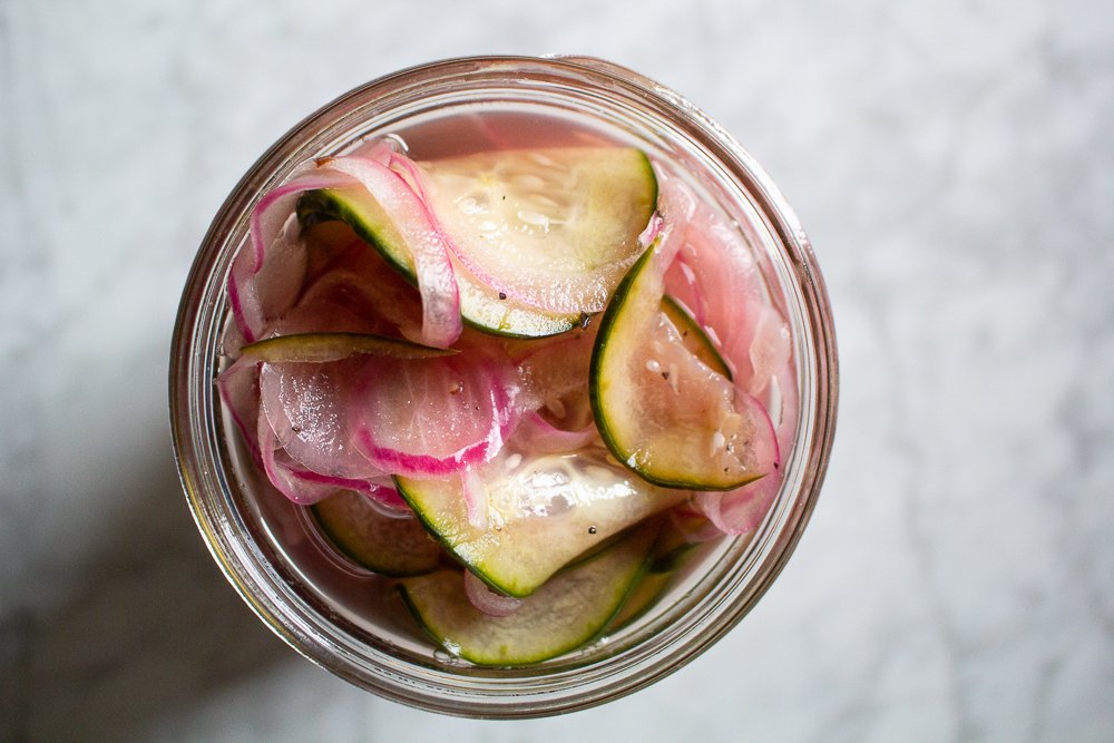 A bowl filled with finely chopped pickles and diced onion on a wooden cutting board, ready to be salted and drained