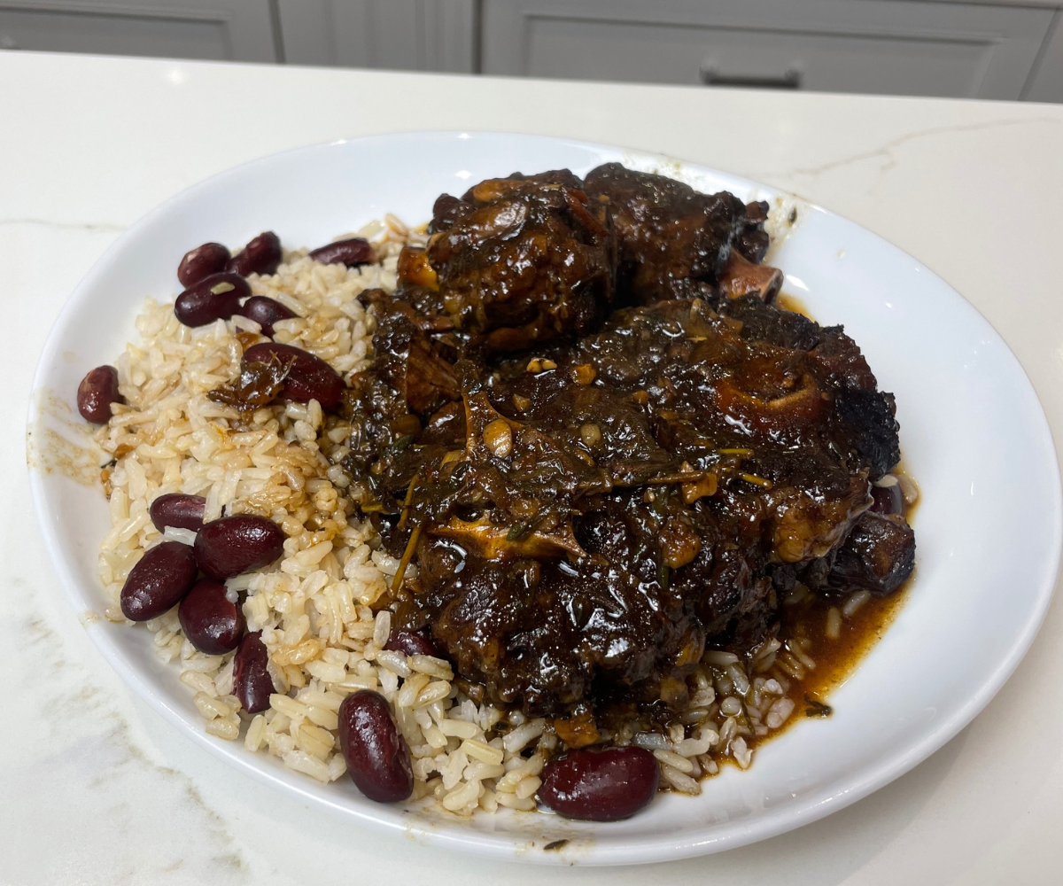 A bowl of Jamaican oxtail with glossy brown gravy and butter beans served over rice, with chopped scallions on top on a warm kitchen table