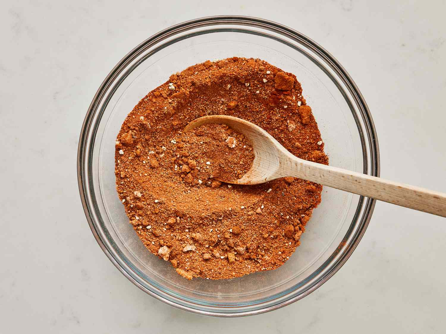 A bowl of brown sugar and spices being mixed into a dry rub with a spoon on a kitchen counter