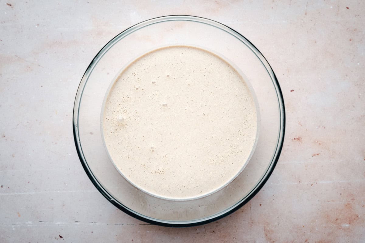 A bowl of buckwheat crêpe batter resting on a kitchen counter with a whisk beside it
