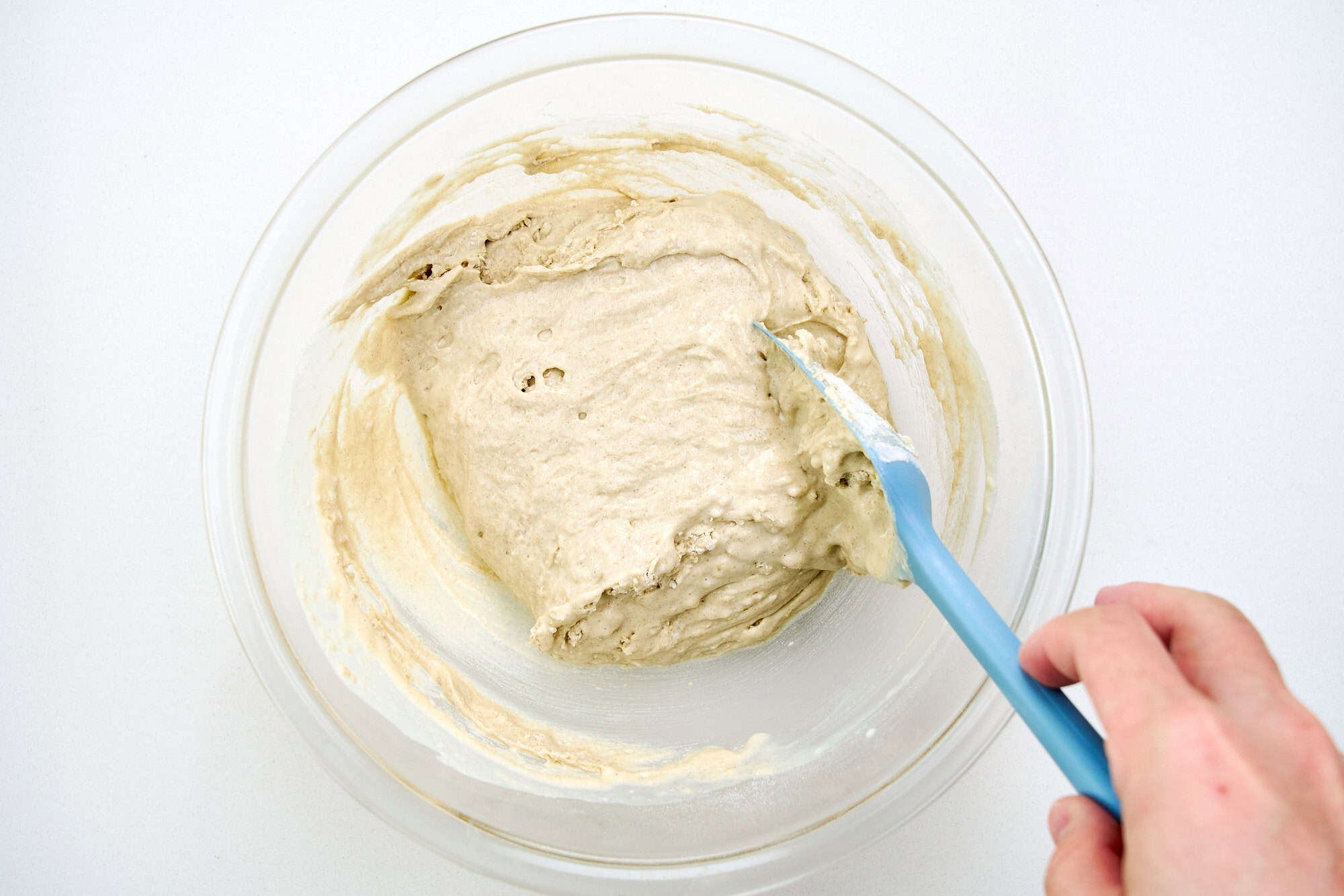 A bowl of buckwheat pancake batter being gently folded with a spatula, with a few small lumps visible on a kitchen counter