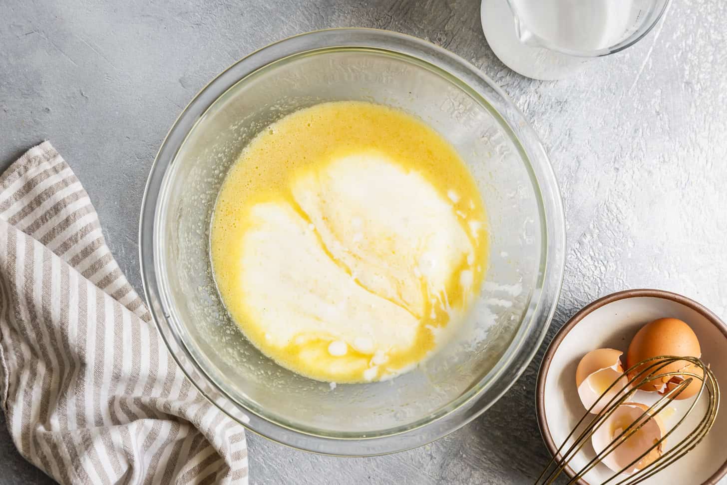A bowl of buttermilk with cracked eggs and melted butter nearby on a kitchen counter, ready to be whisked for cornbread batter