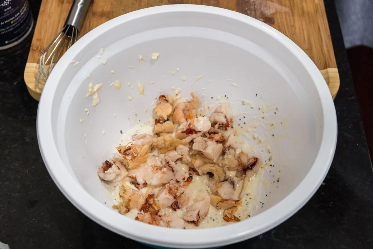 A bowl of chopped cooked lobster meat on a kitchen counter with a knife and cutting board nearby