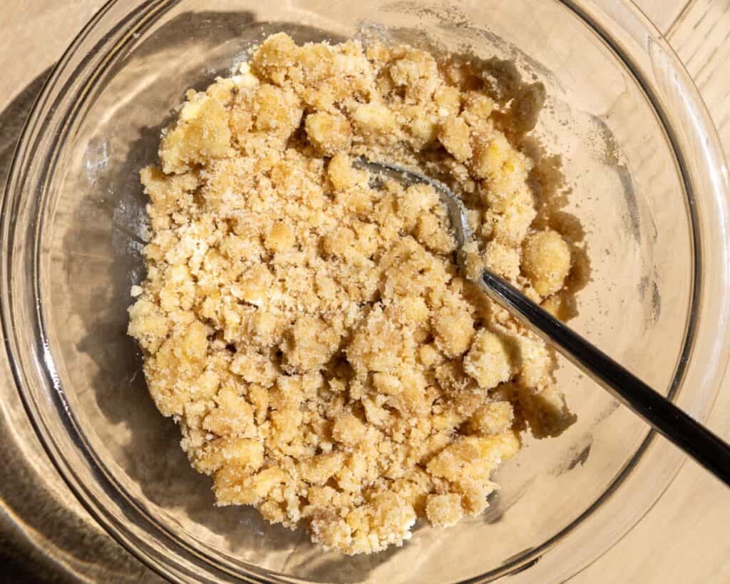 A bowl of cinnamon brown sugar streusel being mixed with melted butter using a fork on a kitchen counter