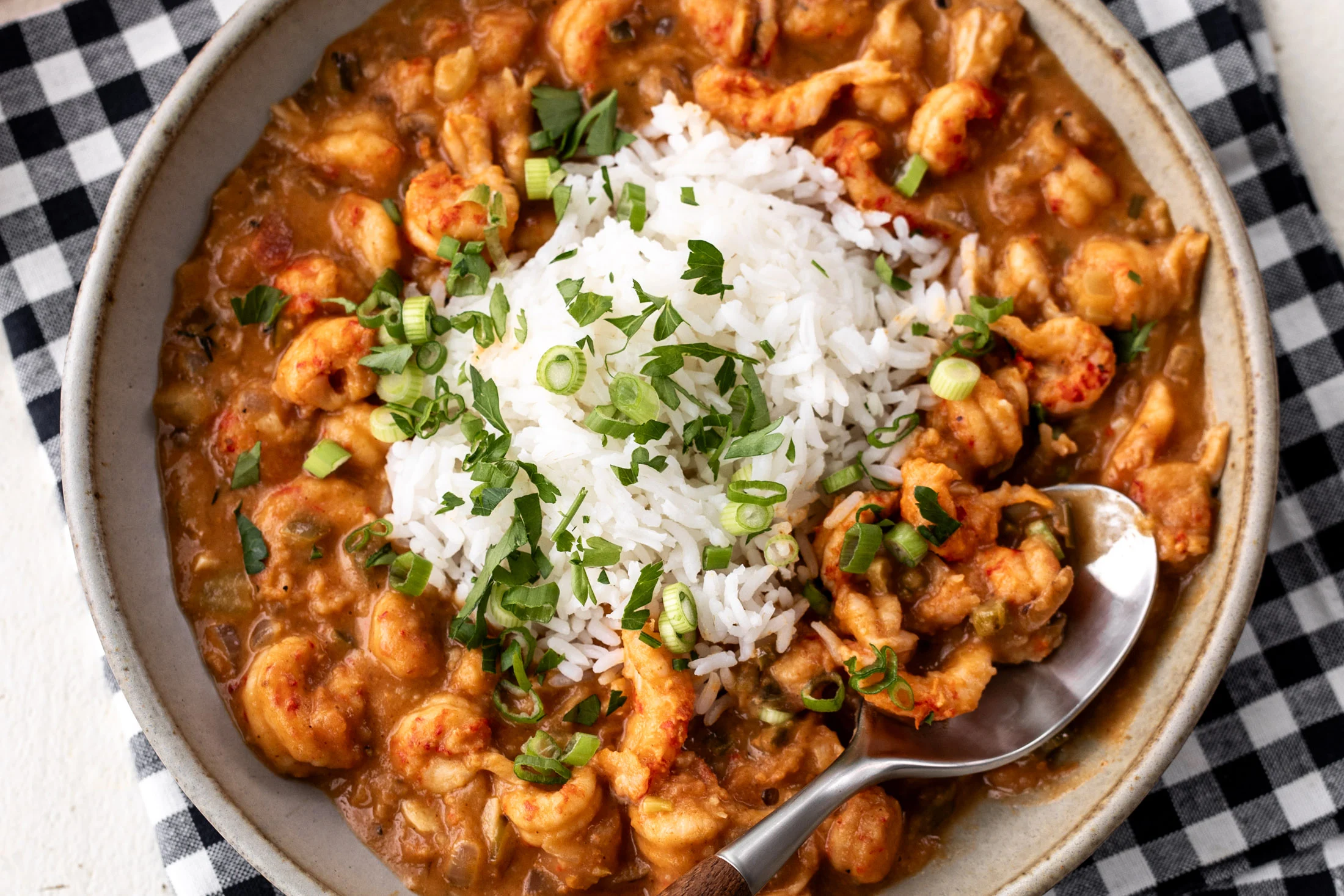 A bowl of crawfish etouffee ladled over white rice, garnished with sliced green onions and parsley on a warm wooden table