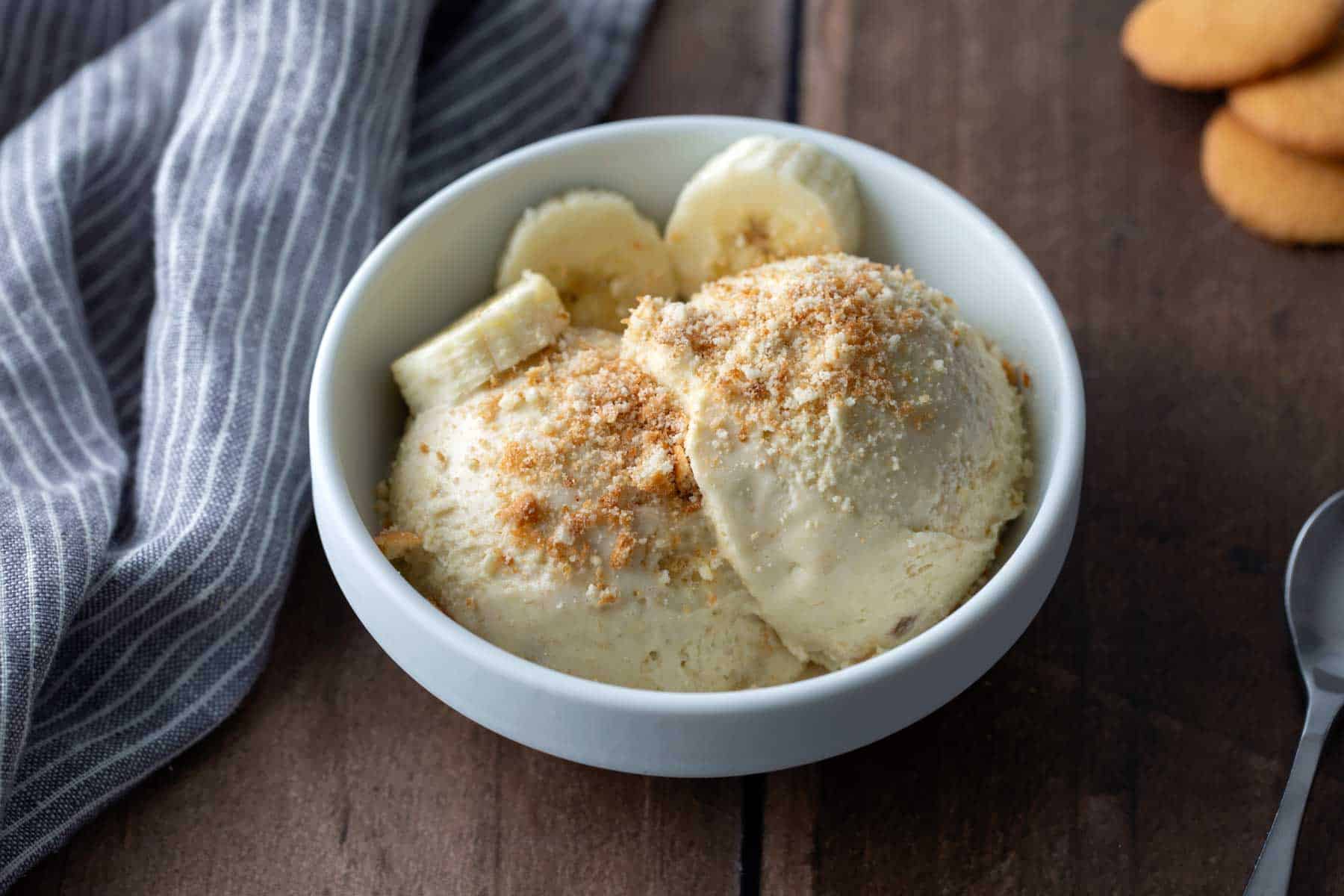 A bowl of creamy banana ice cream topped with banana slices on a light kitchen table with a spoon nearby